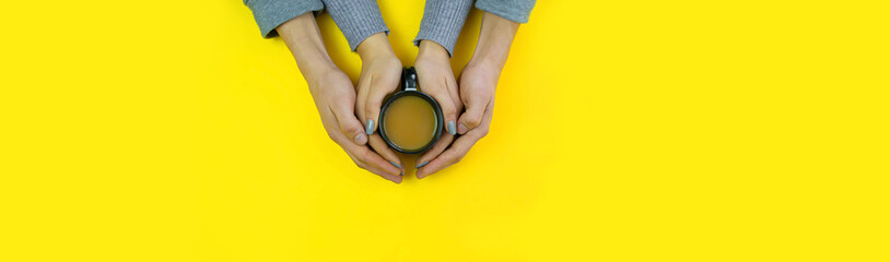 Wall Mural - Hands on a yellow background with coffee, love. Coffee with milk, black cup. Selective focus.