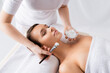 beautician holding cosmetic brush and container with face mask near client with closed eyes lying on massage table