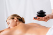 © LIGHTFIELD STUDIOS - masseur holding hot stones near client on blurred background