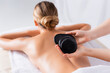 © LIGHTFIELD STUDIOS - cropped view of masseur holding black hot stones near client in spa salon