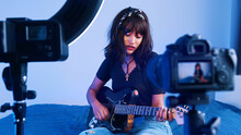 Young Woman Playing Guitar In Front Of The Camera. Recording Demo Or Giving Online Class. High Quality Photo