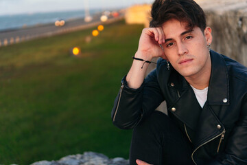 Close-up portrait of a handsome young man sitting and looking at the camera outdoors.