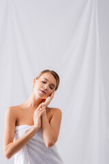 Wall Mural - young woman wrapped in towel touching face on white
