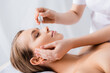 © LIGHTFIELD STUDIOS - beautician holding pipette and applying serum on face of woman with closed eyes in spa salon