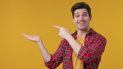 Wall Mural - Smiling excited young man 20s in casual red basic checkered shirt posing isolated on yellow background studio. People lifestyle concept. Point index finger on empty palm showing thumb up like gesture