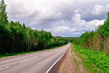 An asphalted intercity road with white markings extending into the distance through a green forest.