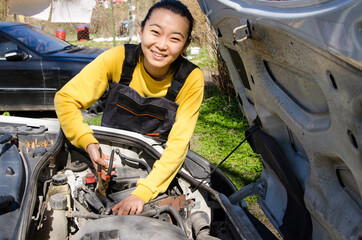 Asian female mechanic dressed in special clothes fixing a car near the house