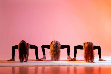 Wall Mural - group of three girls in black tight-fitting suits dancing on red background with their long hair down.