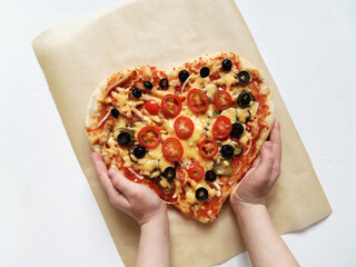 a child holds a heart shaped pizza made with his own hands. February 14 and mom's day holiday concept