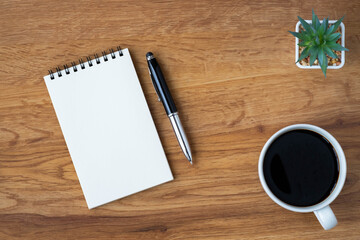 Top view of open school notebook with blank pages, coffee cup and pen for taking write notes on wood table background. Flat lay, creative workspace office. Business-education concept with copy space.