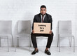 © Prostock-studio - African American man in formal suit holding LOOKING FOR JOB sign, waiting for work interview at office lobby, free space