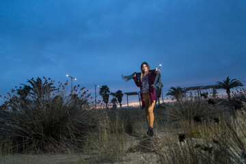 Bella ragazza mora, con maglione color amaranto e sciarpa al collo passeggia vicino alla riva del mare