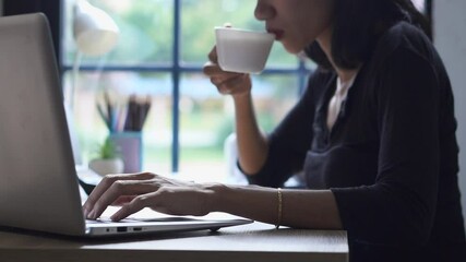Wall Mural - Remote working at Home office Concept. Businesswoman working online via laptop and drink coffee. Asian young entrepreneur watching webinars and talking during meeting video conferences calls with team