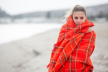 bellissima ragazza bionda si avvolge con una coperta a quadri di colore arancione in una fredda giornata al mare