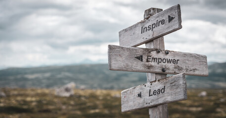 inspire empower lead text engraved on wooden signpost outdoors in nature. Panorama format.