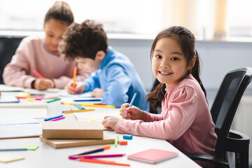 Smiling asian school girl sitting at desk in classroom