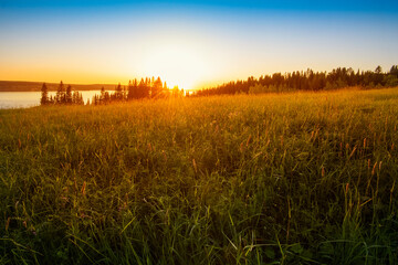 Wall Mural - panoramic view of the kama river from the hill, green meadow, rural road, sunset sky and sun rays.