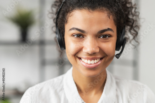 Headshot of friendly African American millennial woman in headset, smiling and working in emergency helpline or in the customer service department as call center operator, helping client with inquiry