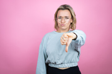 Wall Mural - Young caucasian woman wearing sweatshirt over pink background with angry face, negative sign showing dislike with thumb down