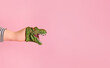 Kid hand wearing funny dinosaur puppet doll on pink background. Dinosaur toy growls roar and speaks. Copy space for advertisements and text promotional content.