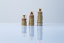 Word "TAX" On Wooden Blocks On Top Of Ascending Stacks Of Coins Against Gray Background. Concept Photo Of Increase Of Taxes, Economy, Business And Finance.