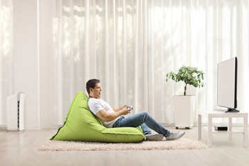 Wall Mural - Young man sitting on a green bean bag and playing video games with a joystick