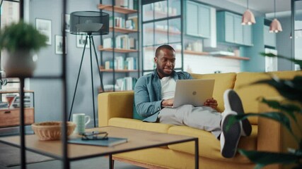 Aufkleber - Handsome Black African American Man Working on Laptop Computer while Lying on a Sofa in Cozy Living Room. Freelancer Working From Home. Browsing Internet, Using Social Networks, Having Fun in Flat.