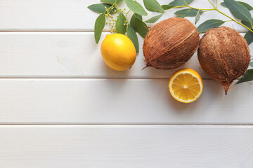 Composition with lemons, coconuts and eucalyptus leaves on a white wooden table with copy space for text. Tropical summer fruits background. Flat lay, top view