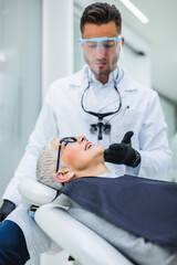 Wall Mural - Beautiful senior woman having dental treatment at dentist's office. Dentist is wearing protective face mask and shield due to coronavirus pandemic..