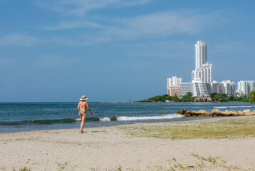 Tall elegant woman walks alone on the sand in her bathing suit on a sunny day.   