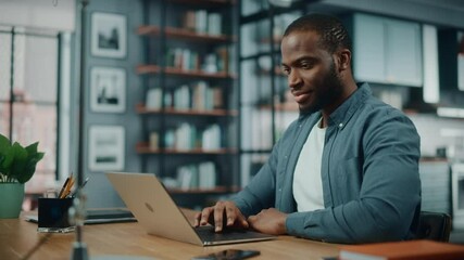 Poster - Handsome Black African American Man Working on Laptop Computer while Sitting Behind Desk in Cozy Living Room. Freelancer Working From Home. Browsing Internet, Using Social Network, Having Fun in Flat.