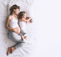 Pregnant mother and daughter resting in bed. Young woman with her first child during second pregnancy. Motherhood and parenting concept.