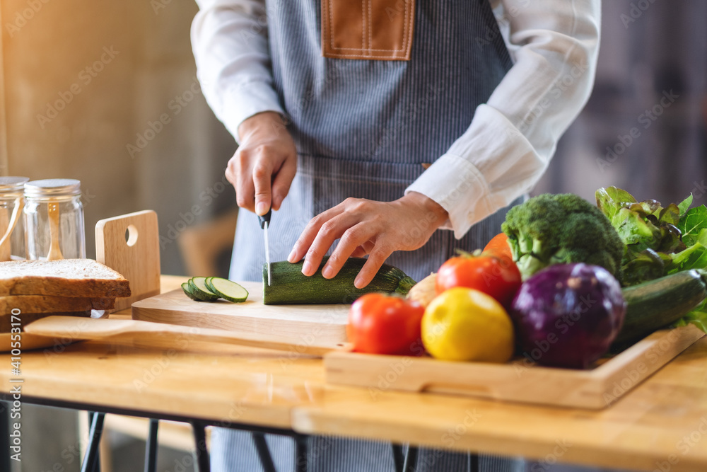 Closeup image of a female chef cutting and chopping vegetables by knife on wooden board in kitchen - obrazy, fototapety, plakaty 