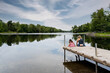Young mother and daughter sitting on edge of a wooden deck with their backs to the camera looking in to the water, lake at Almonte, Ontario.