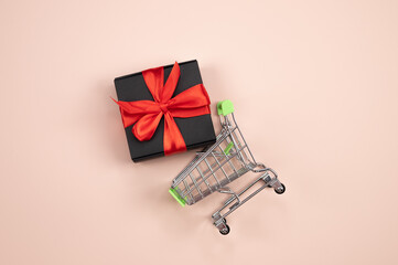 Black gift box tied with red ribbon in a shopping cart. Cart with purchases. Present concept.