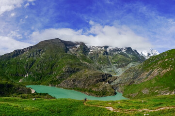 hydroelectric power plant in the mountains with green water and hikers panorama