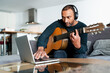 © SYCprod - Black man playing the guitar at home and using a laptop