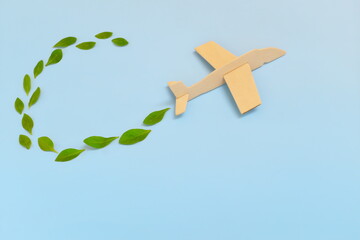 Wooden airplane model emitting fresh green leaves on blue background. Sustainable travel; clean and green energy; and biofuel for aviation industry concept.