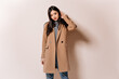 © Look! - Beautiful Asian woman looking confidently into camera. Girl in beige coat posing on isolated background