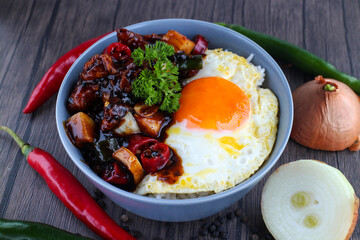 Wall Mural - Rice in a bowl with sunny side up and fried chicken with black pepper sauce. Wooden background, chilies and onions.