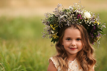 Wall Mural - Cute little girl wearing wreath made of beautiful flowers in field