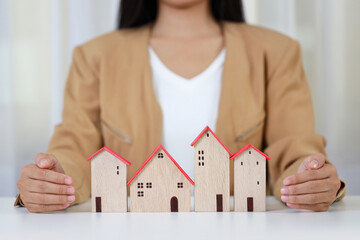 Young active business woman hands in casual dress sitting and protecting house model on white table. Property insurance and security concept