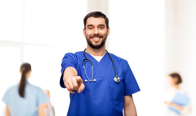 Sticker - healthcare, profession and medicine concept - happy smiling doctor or male nurse in blue uniform with stethoscope pointing finger to camera over hospital on background