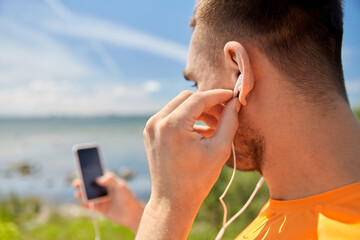 Sticker - fitness, sport and technology concept - young man with smartphone and earphones listening to music at seaside in summer