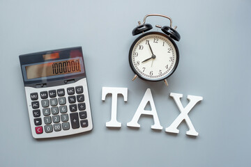 TAX text with calculator and alarm clock on gray background. investment and time to tax concepts