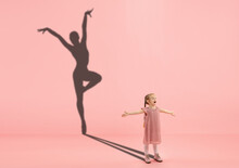 Childhood And Dream About Big And Famous Future. Conceptual Image With Girl And Drawned Shadow Of Female Ballet Dancer On Coral Pink Background. Childhood, Dreams, Imagination, Education Concept.