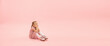 Dreamful baby. Childhood and dream about big and famous future. Pretty girl on coral pink studio background. Childhood, dreams, imagination, education, facial expression, emotions concept. Flyer