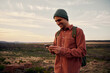 © StratfordProductions - Happy male hiker with backpack and cap using smartphone on mountain
