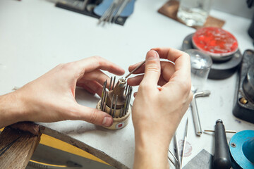 Wall Mural - Leveling. Close up hands of jeweller, goldsmiths making of golden ring with gemstone using professional tools. Craft production, precious and luxury jewel, hand made occupation. Workshop, artwork.