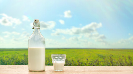 Bottle and glass with fresh milk on a background of green meadow and blue sky